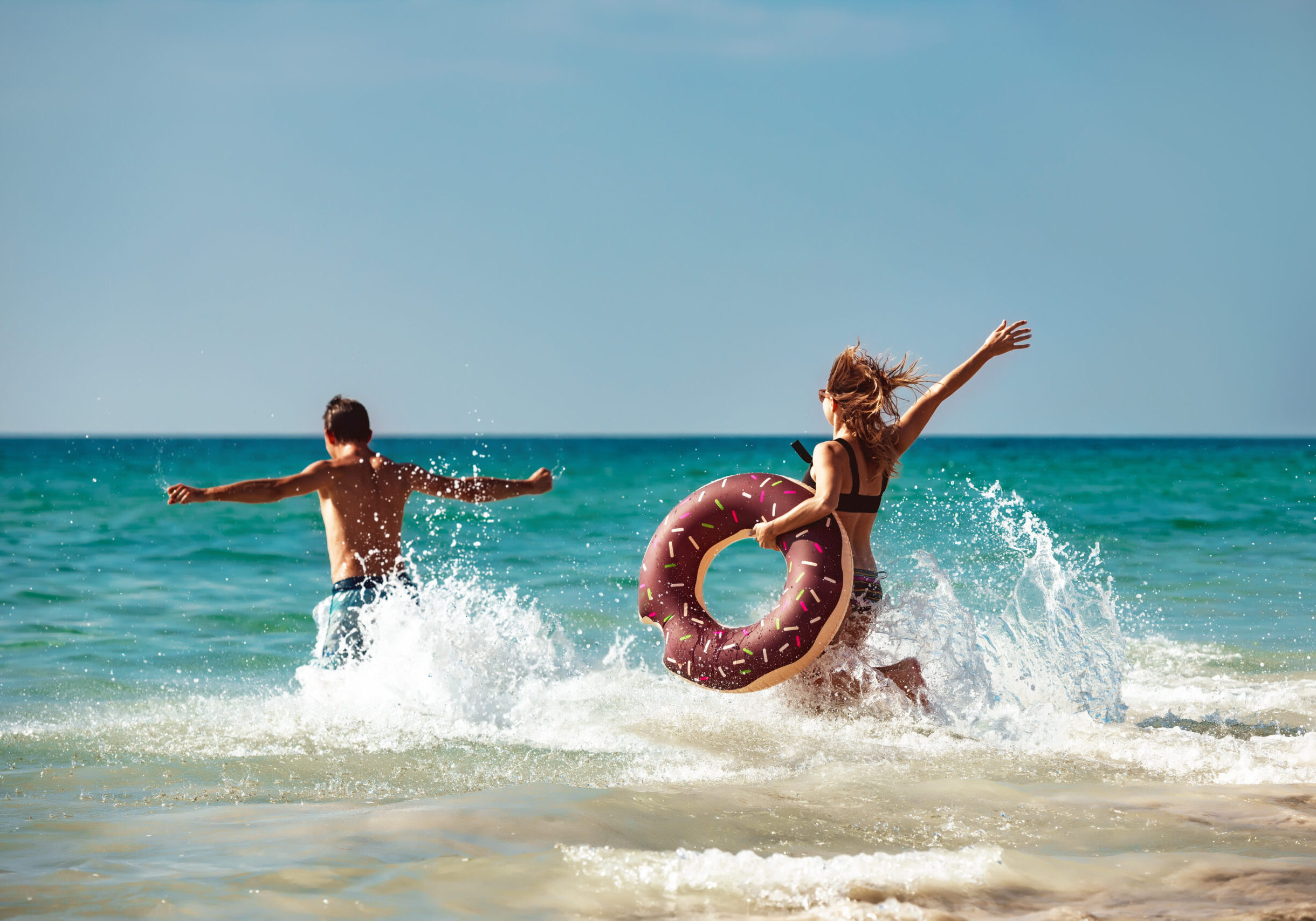 Happy young couple are having fun with inflatable donut at sea beach. Tropical vacations concept